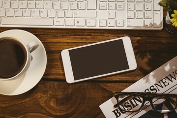 overhead white smartphone on wooden desk showing keyboard, coffee, newspaper, glasses, potted plant