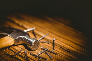 Hammer with wooden handle is lying flat on workbench in 3D render, with scattered steel nails