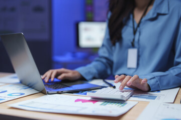 Businesswoman working with calculator and laptop in modern office at night