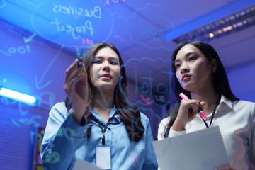 Businesswomen planning project, brainstorming and writing on transparent board