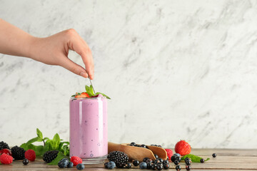 Female hand with glass of fresh smoothie and different berries on wooden table