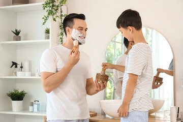 Happy father and his little son with brushes applying shaving foam on their faces in bathroom