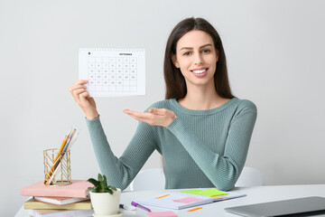 Beautiful young happy woman pointing at calendar in office