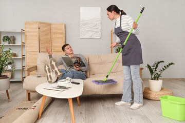 Lazy husband reading magazine while his wife mopping at home