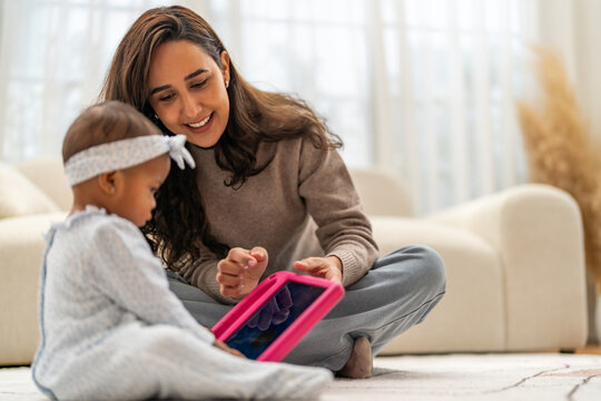 African mother sitting on floor showing tablet to her baby daughter at home, spending time learning together, enjoying digital bonding moment, early childhood development and african family lifestyle