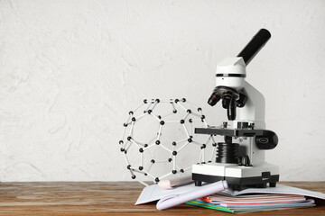 Modern microscope with copybooks and molecular model on wooden table against white grunge background