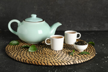 Cups and teapot of hot tea with dried leaves on black background