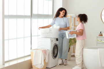 African-American woman and her daughter doing laundry in bathroom