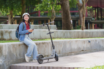 Young woman using smartphone while relaxing next to electric scooter in park © crizzystudio