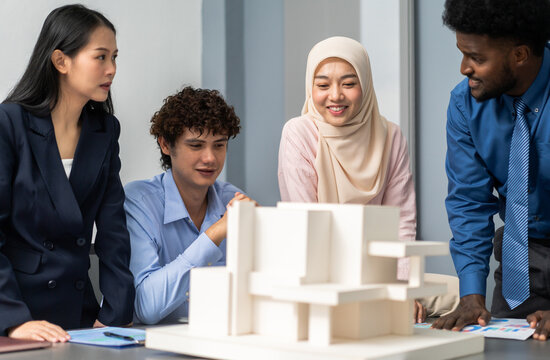 Architects engineers collaborating on building design project in modern office, diverse team of professionals female muslim architect and male engineers discussing architectural model of structure