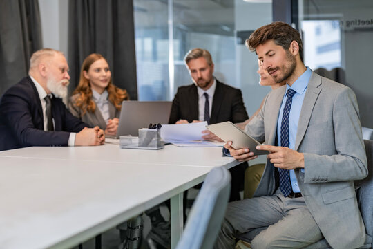 Portrait of adult businessman sitting at his desk in the office and smiling looking at digital tablet - Powered by Adobe