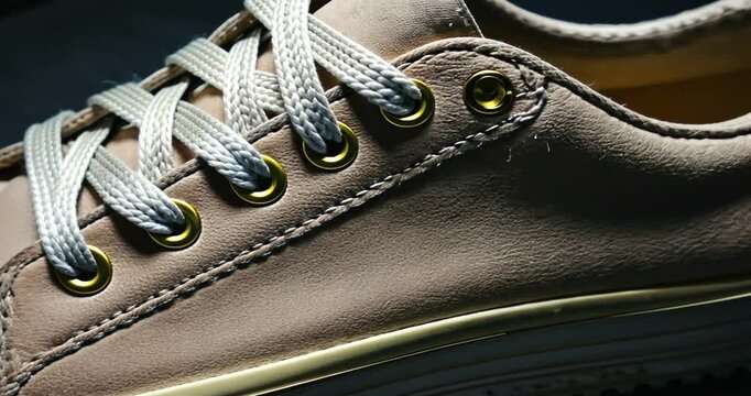 Close-up of a stylish beige sneaker showcasing intricate stitching and eyelets on a textured surface
