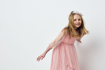 Joyful young girl in a pink dress with a crown, expressing happiness in a minimalist studio...