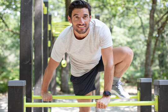muscular man jumping pull-ups on horizontal bar in park