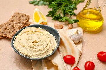 Bowl of tasty hummus with ingredients, crackers and napkin on beige grunge background, closeup