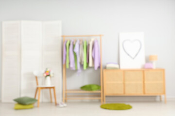Blurred view of light dressing room with different female clothes and spring flowers