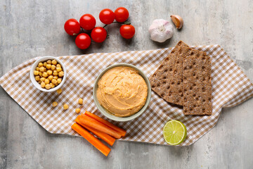 Bowl of tasty hummus with carrot, tomatoes and crackers on grey grunge background
