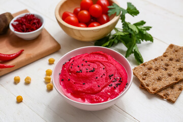Bowl of tasty beet hummus with tomatoes, parsley and crackers on white wooden background