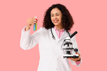 Female African-American doctor with microscope and test tubes on pink background