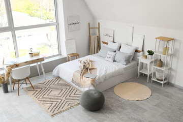 Interior of light bedroom with comfortable bed, pouf and workspace near window
