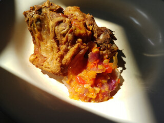Close-Up of Crispy Fried Chicken with Spicy Red Sambal on White Plate in Natural Sunlight