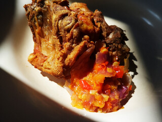 Close-Up of Crispy Fried Chicken with Spicy Red Sambal on White Plate in Natural Sunlight