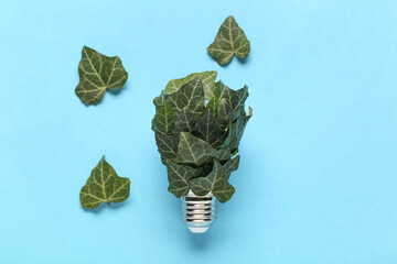 Light bulb with plant leaves on blue background. Green technology concept