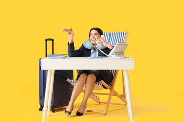 Young businesswoman with wooden airplane talking by telephone in deck chair at table on yellow...