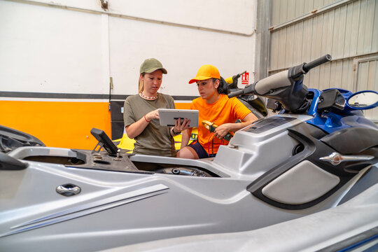Female mechanics repairing personal watercraft with digital tablet in workshop