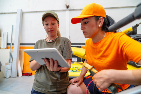 Female mechanics using digital tablet while repairing motorbike in garage - Powered by Adobe