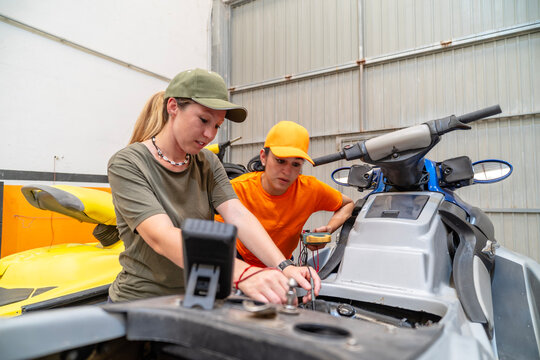 Two mechanics repairing personal watercraft engine in workshop