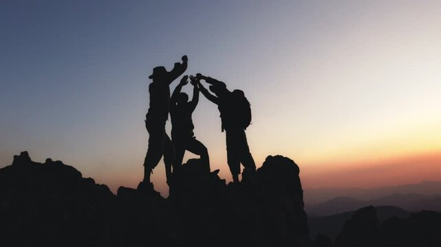 Silhouette of people hiking to the mountain and giving high fives on top of mountain and raising her hands celebrating successful