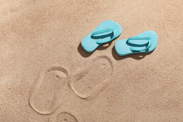 Decorative flip-flops and footprints on sand as background, closeup
