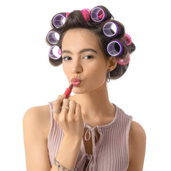 Young woman with hair curlers applying lipstick on white background, closeup