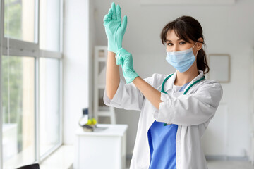 Female medical intern with mask and gloves near window in clinic