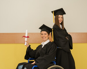 Happy young woman and woman in wheelchair in graduate gown with diploma in hands. Inclusive...