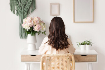 Young woman with bouquet of peony flowers on desk at home, back view © Pixel-Shot