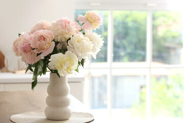 Vase with bouquet of beautiful peonies on table in kitchen, closeup