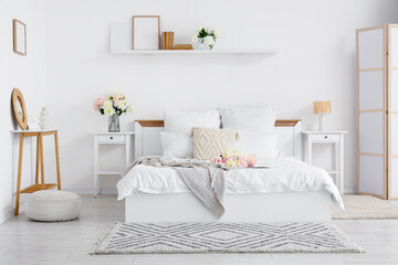 Interior of stylish bedroom with cozy bed and beautiful peonies