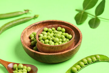 Wooden bowls and spoon with fresh green peas on color background, closeup