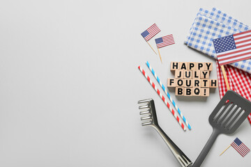 USA flags, wooden cubes with text HAPPY JULY FOURTH BBQ and barbecue utensils on white background....