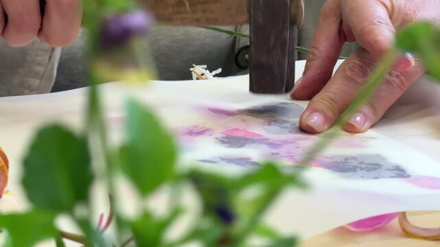 Botanical hammer art in action &ndash; flower pigments visible through parchment, wooden hammer resting on top during floral printmaking process