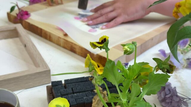 Botanical hammer art in action &ndash; flower pigments visible through parchment, wooden hammer resting on top during floral printmaking process