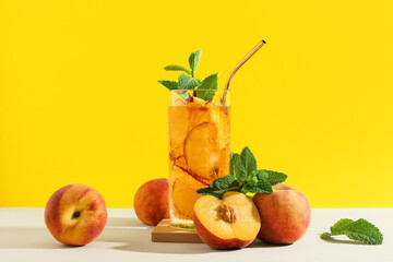 Glass of tasty iced tea with mint and peaches on beige table against yellow background