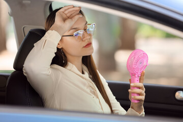 Young woman with mini electric fan suffering from heat in car