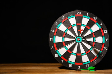 Board with darts on wooden table against dark background