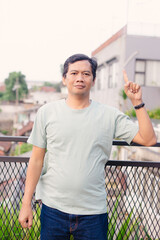 Confident middle-aged man points upwards on a balcony, expressing an idea or insight, outdoor scene