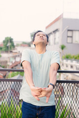 Man stretching outdoors on a balcony looking upward feeling relaxed, calm and refreshed