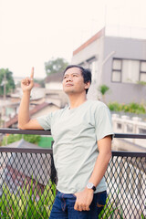 Asian Man Points Upward on Balcony Demonstrating Concept Against Urban Backdrop Focus