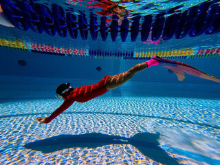 Young woman with mermaid tail swims and dives under sunlit deep water